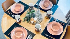 A round wooden dining table with pink plates, black napkins, and matching cutlery. - Aintree On The  Park (Mount Maunganui)