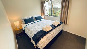 A neatly made bed with a patterned bedspread, two pillows, and a folded towel on a dark carpeted floor. - Aintree On The  Park (Mount Maunganui)