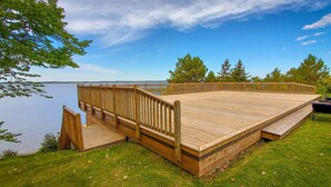 Una terraza de madera con una rampa que lleva a una zona verde junto a un lago.