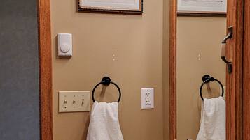 Un baño con un espejo de marco de madera, un lavamanos con grifo dorado, dos toallas blancas y un certificado enmarcado en la pared.