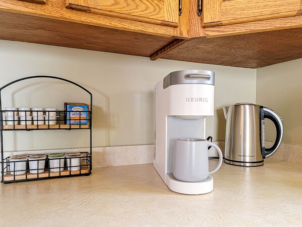 Una cocina con una cafetera Keurig, un hervidor Hamilton Beach y un estante metálico con recipientes.