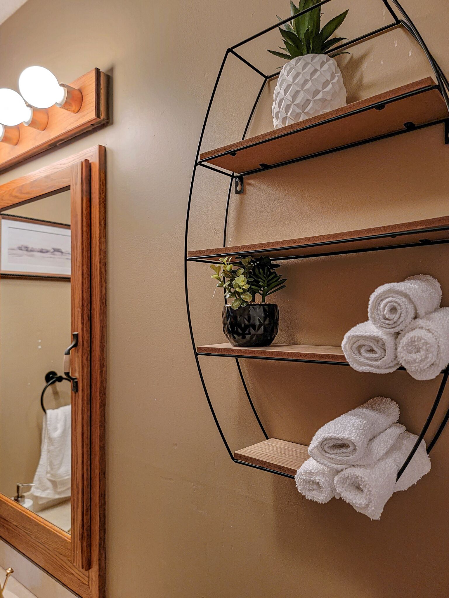 Une salle de bain avec un miroir, un porte-serviettes et une étagère contenant des serviettes et un ananas.