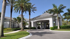 A white building with a covered entrance and palm trees. - First-Floor Carriage House at Colonial CC, Renovated Golf Course with Lake View (Fort Myers)