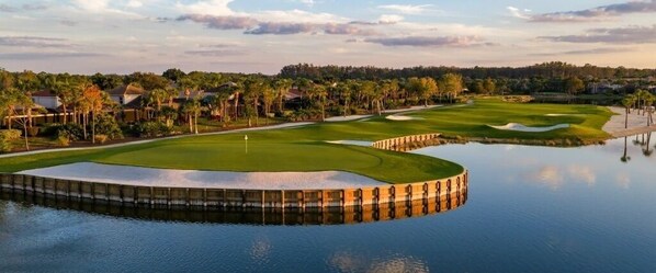 Ein Golfplatz mit einem Wasserhindernis, umgeben von Bäumen und Häusern.