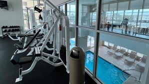 A gym with exercise equipment, a pool, and large windows offering a view of the outside.