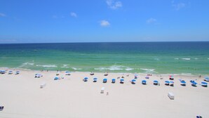 A beach with numerous umbrellas and beach chairs, a clear sky, and the ocean in the background.