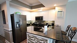 A modern kitchen with white cabinets, a stainless steel refrigerator, a microwave, and a built-in oven.