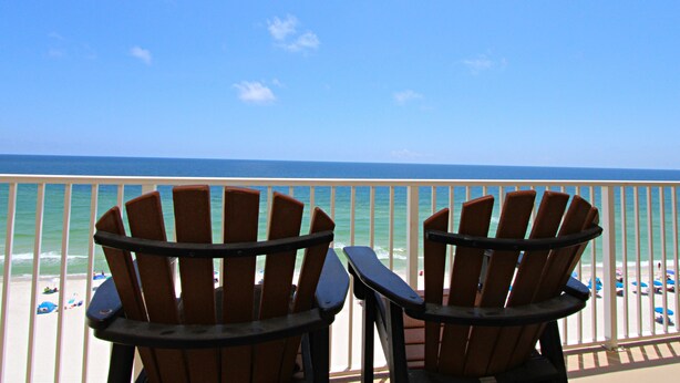 Two Adirondack chairs facing a beach with umbrellas and a view of the ocean.