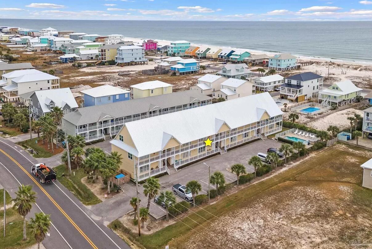 A coastal residential area with colorful houses, a large building with a white roof, and a beach in the background.