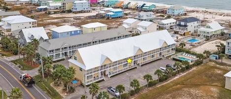 A coastal residential area with colorful houses, a large building with a white roof, and a beach in the background.