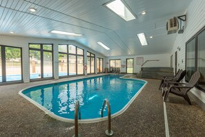An indoor swimming pool with clear glass walls, a tiled floor, and a ceiling with skylights.