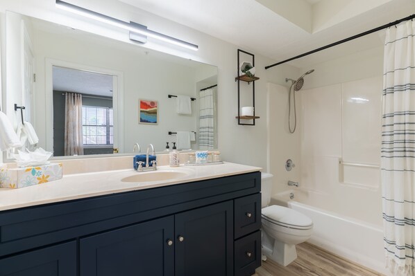 A modern bathroom with a large mirror, a sink with toiletries, a toilet, and a shower area.