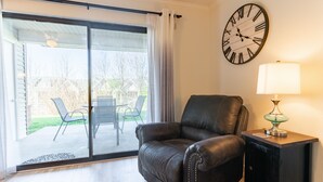 Uma sala de estar com um sofá de couro, um relógio de parede, um abajur e uma porta de vidro deslizante para um alpendre.