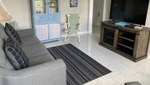 Una sala de estar con un sofá gris, un armario azul, un mueble de madera para entretenimiento y un televisor.