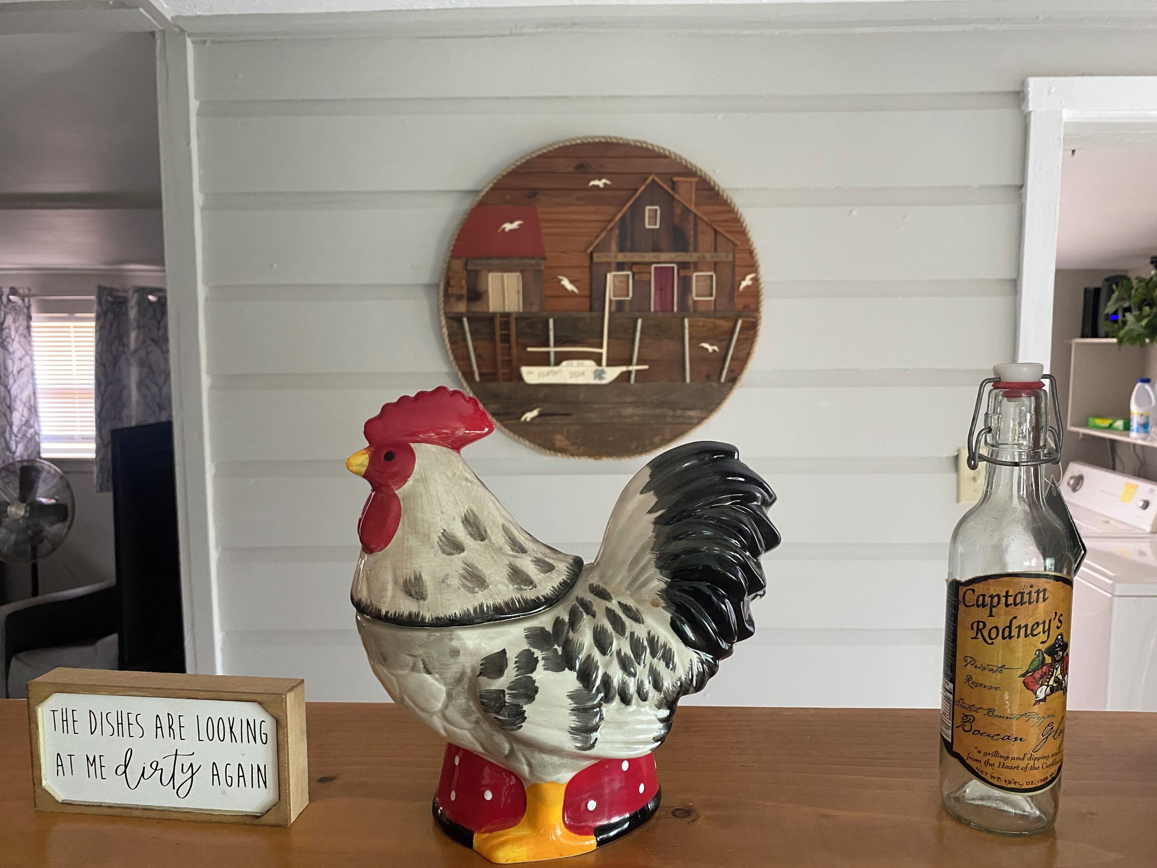 A ceramic rooster, a bottle of Captain Rodney's Boccane, and a sign with text.