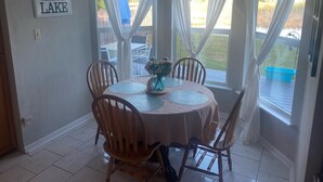 Un comedor con una mesa redonda, cuatro sillas de madera, un florero con flores y un cartel que dice "welcome to the LAKE".