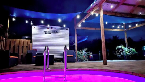 Ein Poolbereich mit einem Wohnmobil im Hintergrund, umgeben von einer Holzterrasse und Lichterketten.