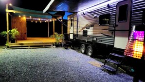 Ein Wohnmobil vor einem Haus mit überdachter Veranda und Sitzgelegenheit im Freien.