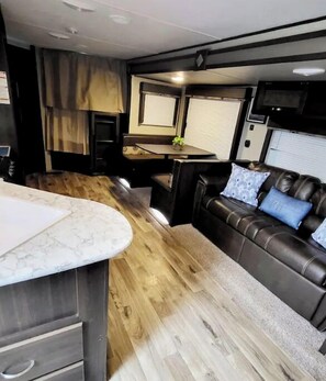 Interior compacto de autocaravana con cocina, zona de estar con sofá de cuero y una pequeña mesa.