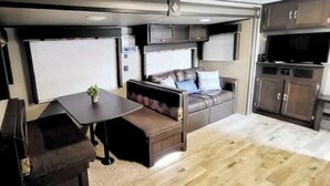 Ein kompaktes Wohnmobil-Interieur mit einer Sitzecke, einem kleinen Tisch, einem Fernseher und einer Küchenzeile.