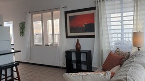 Un salon comprenant un canapé, une table basse, un tableau et une vue sur la mer, visible à travers une porte coulissante.