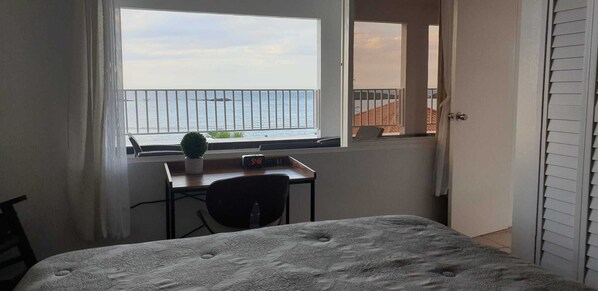 A bedroom with a bed, a desk with a chair, a small potted plant, and a window with a view of the sea. - Mare Blu beach apt + private oceanfront terrace (Vega Baja)