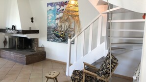 A living room with a fireplace, a wooden chair, a small stool, and a staircase.