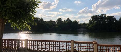A view of a lake with a wooden fence and trees in the foreground.