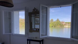 A room with two open windows, a bed, a small table, and a mirror.