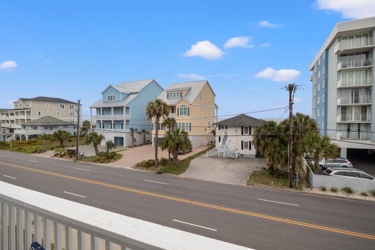 A coastal residential area with multi-story buildings, a clear sky, and a road with no visible traffic.