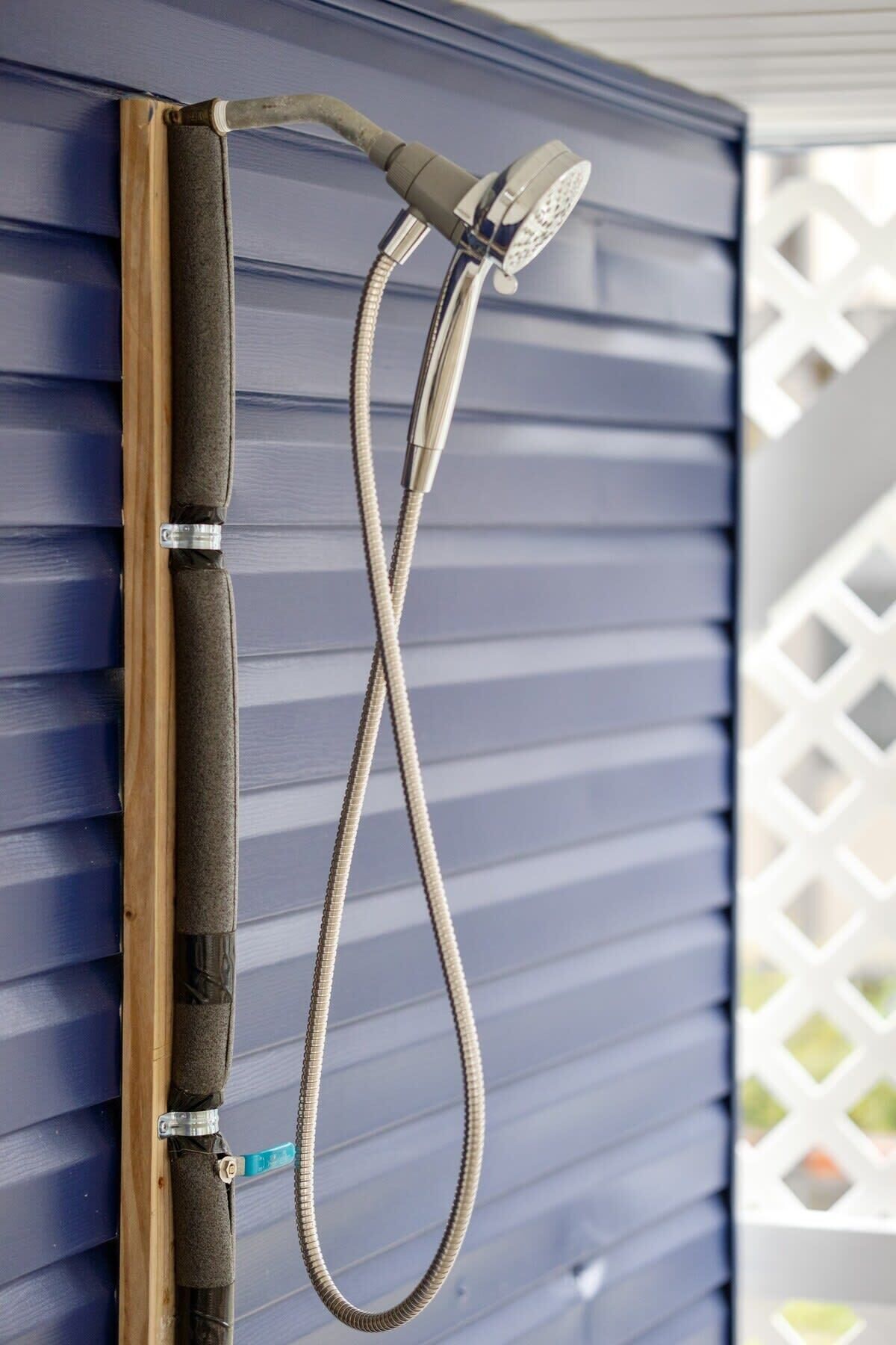 Un tuyau de douche fixé à un poteau en bois, adossé à un mur extérieur bleu.