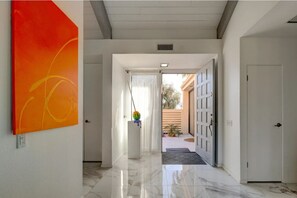 Experience a contemporary space with a large abstract art piece, a hallway leading to an outdoor area, and a sleek, reflective floor.