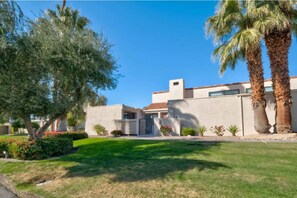 Stucco and concrete building with a flat roof, surrounded by lush landscaping and palm trees.