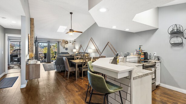 A modern kitchen with a bar area, wooden flooring, and a dining area with chairs and a table.