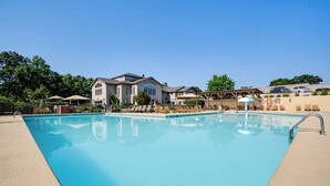 A swimming pool with lounge chairs and umbrellas, surrounded by buildings with a clear blue sky above.