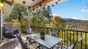A wooden deck with a table and chairs, a hanging chair, and a view of a valley.