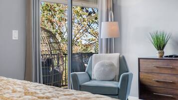 Et soveværelse med seng, stol, kommode og udsigt til en balkon med stol og plante.