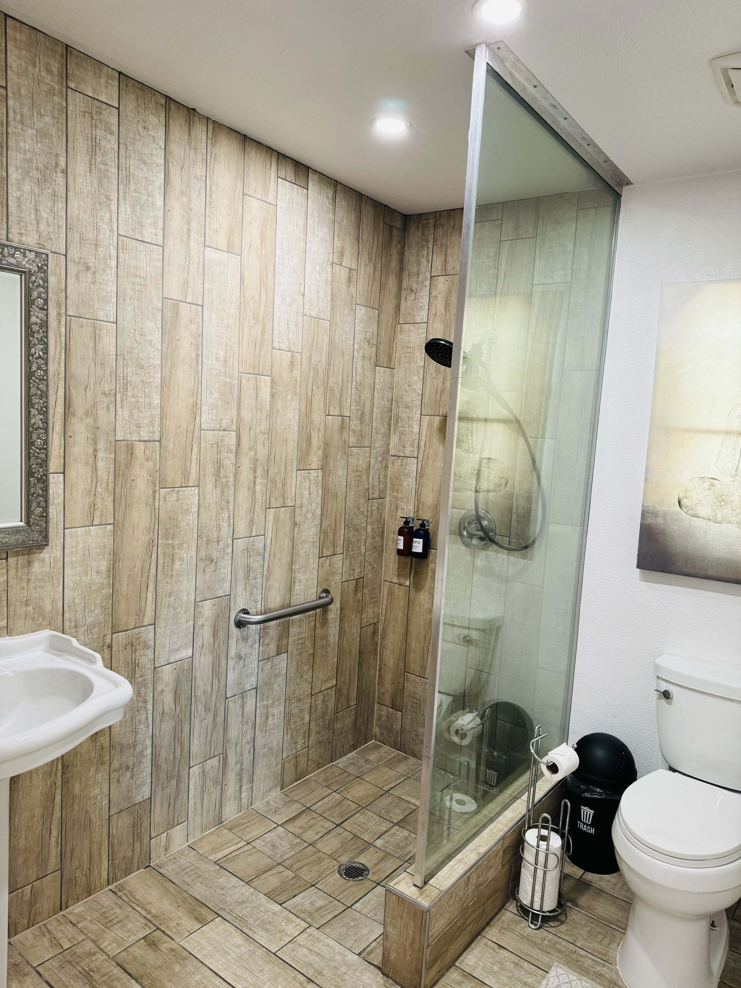 A bathroom with a shower, sink, toilet, and a trash bin.