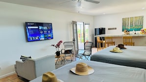 Quarto de hotel com duas camas, uma televisão presa na parede, área de refeições com mesa e cadeiras, e um quadro na parede.