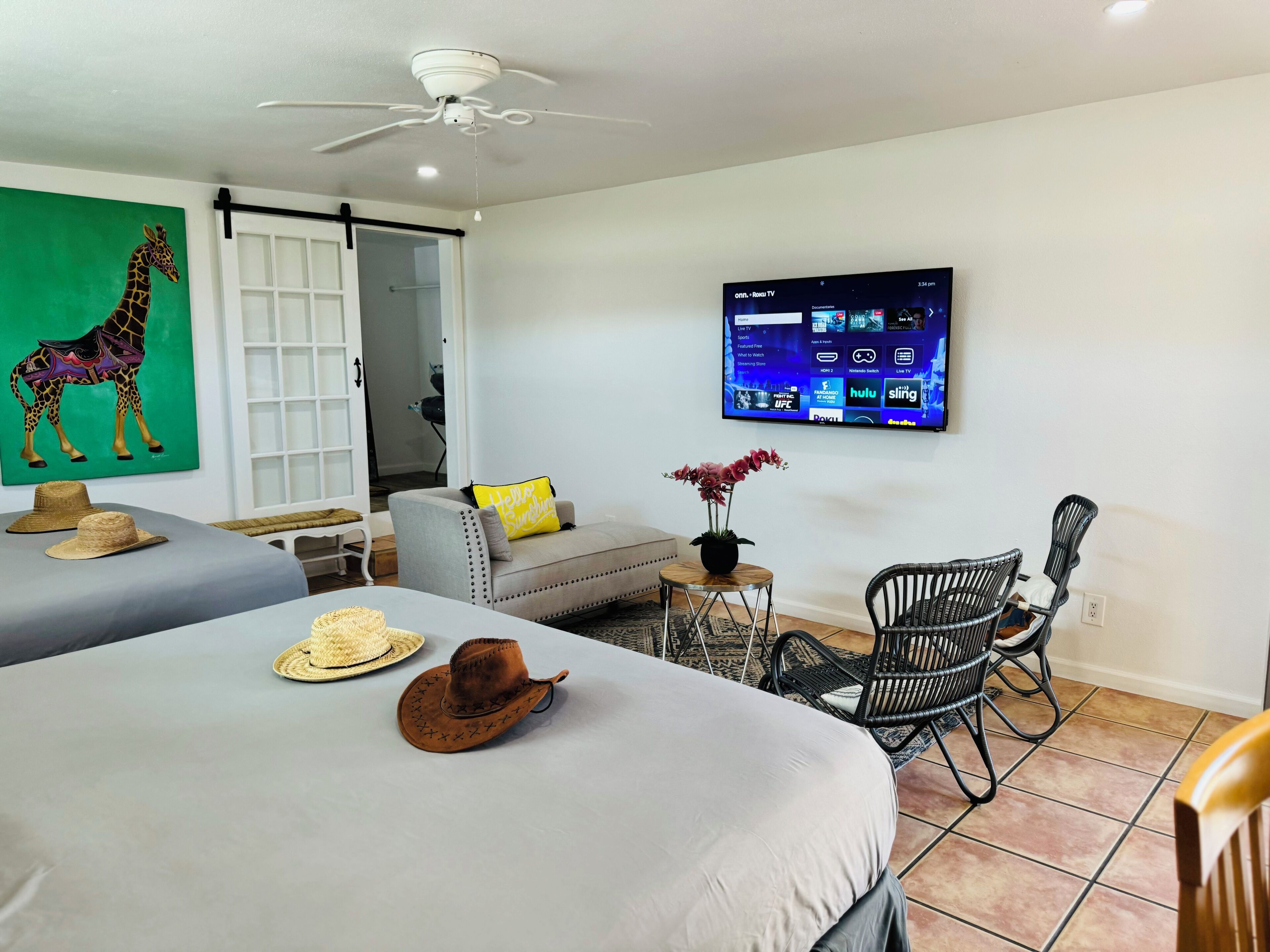 Une chambre d’hôtel avec deux lits, une télévision, un ventilateur de plafond, un canapé et un coin repas avec des chaises.