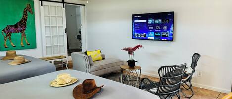 A hotel room with two beds, a TV, a ceiling fan, a sofa, and a dining area with chairs.