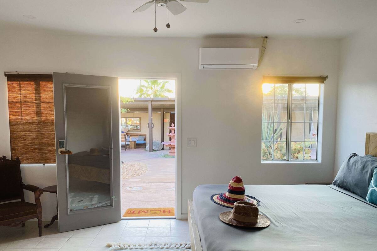 Une chambre avec un lit, une fenêtre, un appareil de climatisation et une porte donnant sur une terrasse.