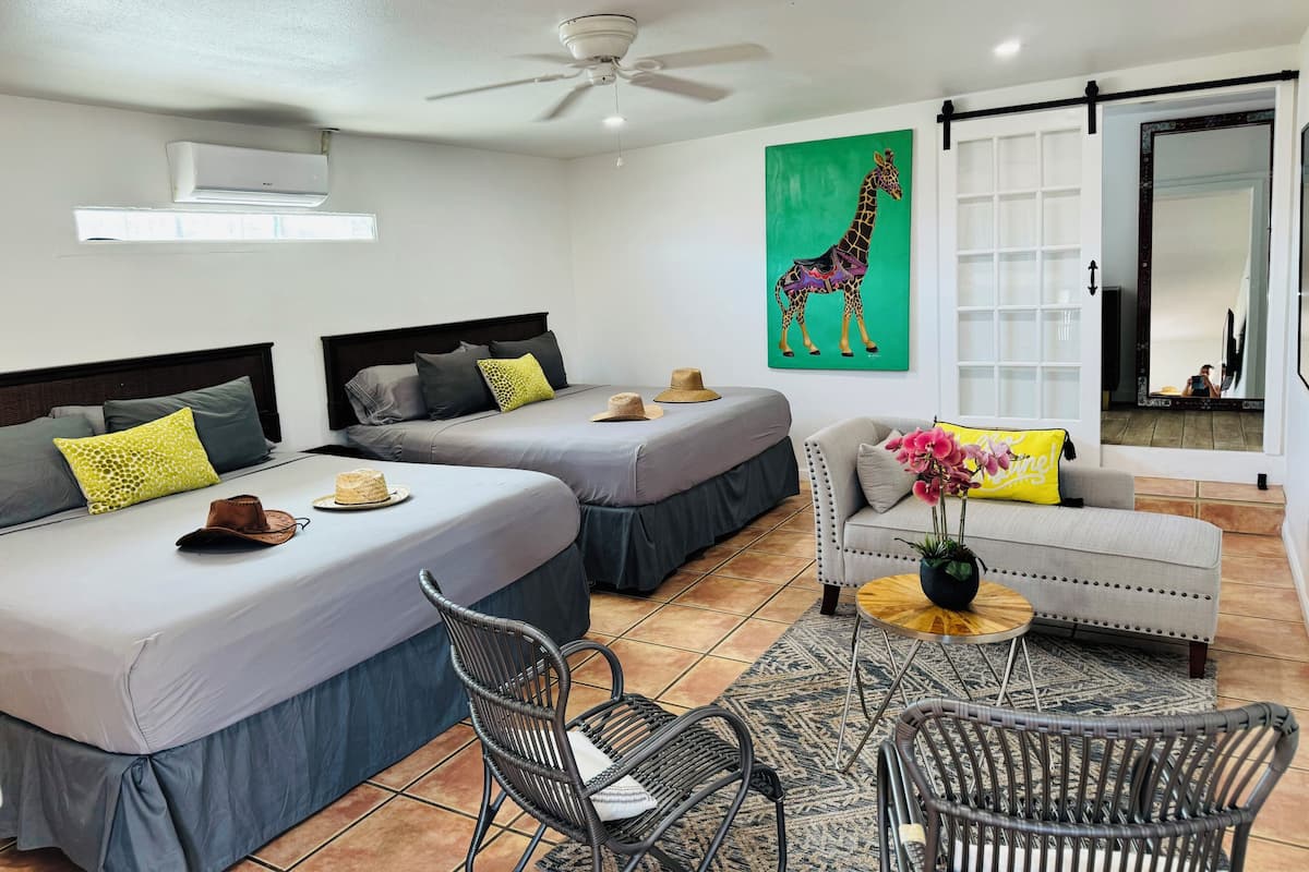 Une chambre d’hôtel avec deux lits, un canapé, un fauteuil, un ventilateur de plafond et un tableau représentant une girafe.