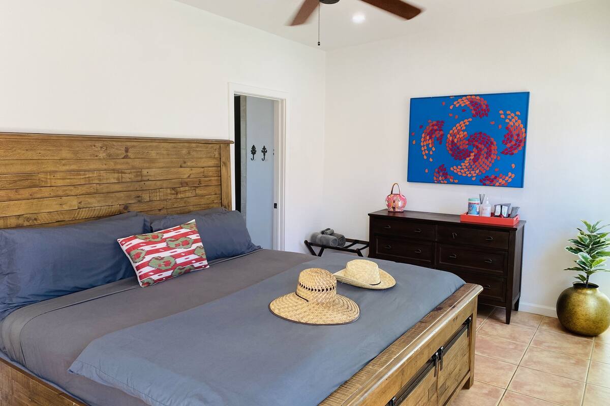 Une chambre avec une tête de lit en bois, une literie grise, une décoration murale bleue, une commode en bois et une plante en pot.