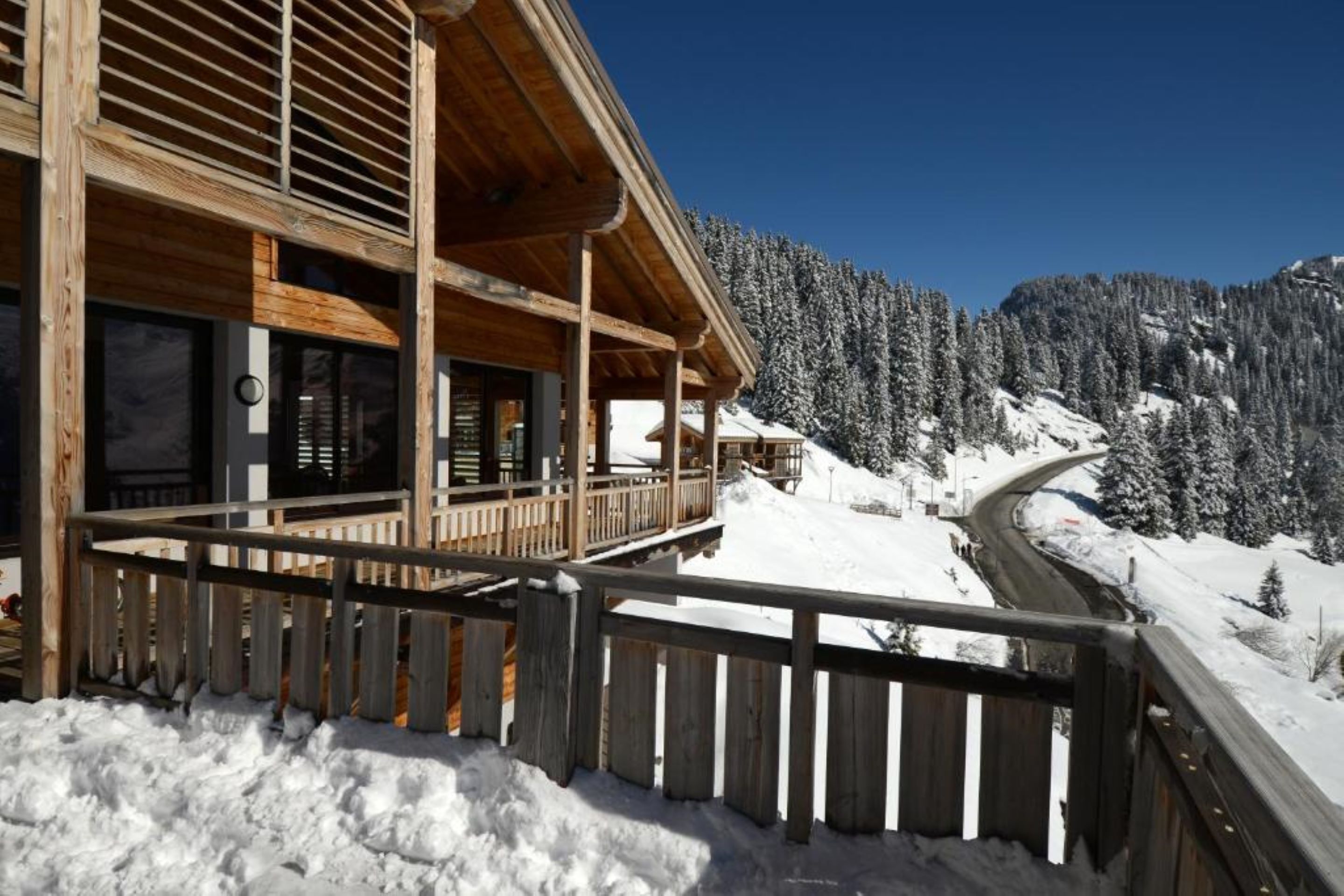 Une cabane en bois dotée d’un balcon donnant sur un sentier de montagne enneigé.