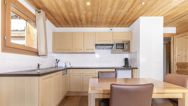 A modern kitchen with wooden cabinets, a built-in microwave, and a dining area with a wooden table and chairs. - Residence Les Portes du Grand Massif – Flaine (Araches-la-Frasse)