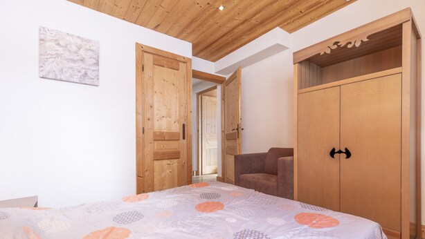 A bedroom with a bed, a wooden wardrobe, and a door leading to another room. - Residence Les Portes du Grand Massif – Flaine (Araches-la-Frasse)