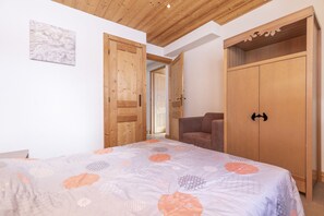 A bedroom with a bed, a wooden wardrobe, and a door leading to another room. - Residence Les Portes du Grand Massif – Flaine (Araches-la-Frasse)