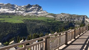 A wooden deck with a view of a mountainous landscape, including a forested valley and rocky peaks. - Residence Les Portes du Grand Massif – Flaine (Araches-la-Frasse)