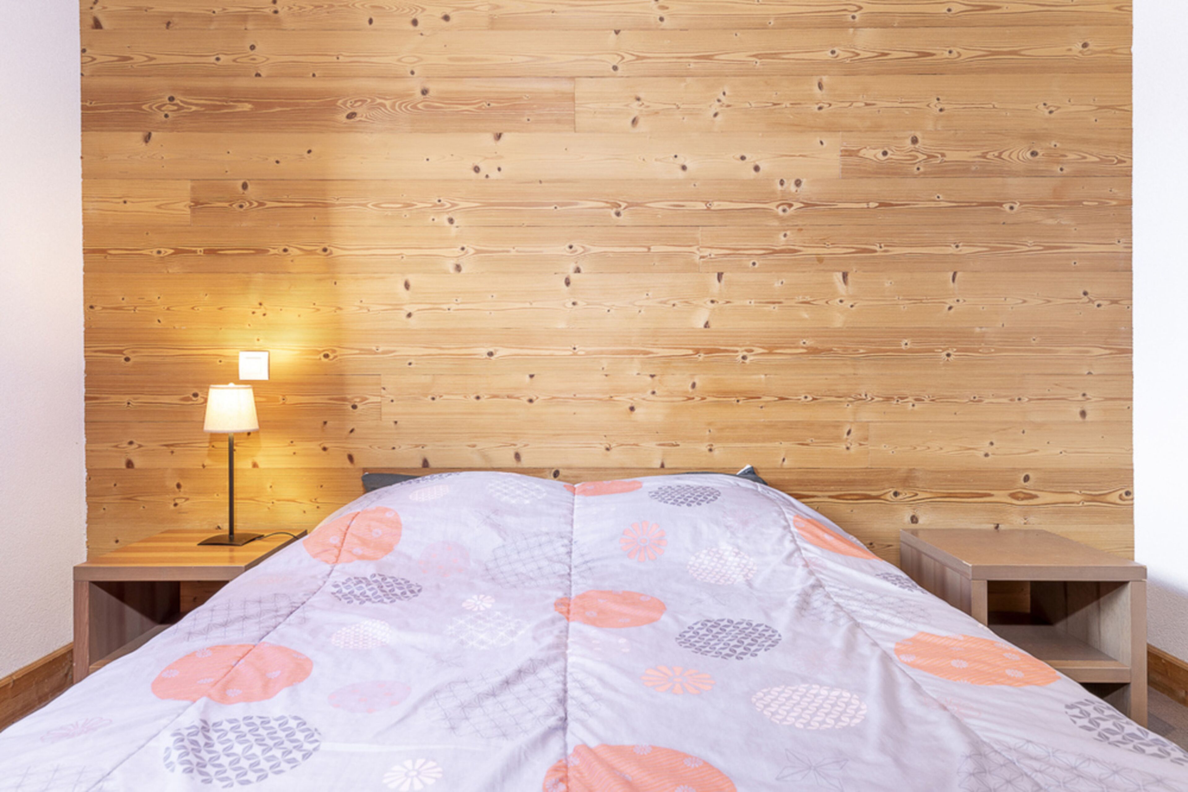 Ein Schlafzimmer mit einem Holz-Kopfteil, einem Bett mit einem gemusterten Überwurf, einem Nachttisch mit einer Lampe und einem zusätzlichen Nachtschränkchen.